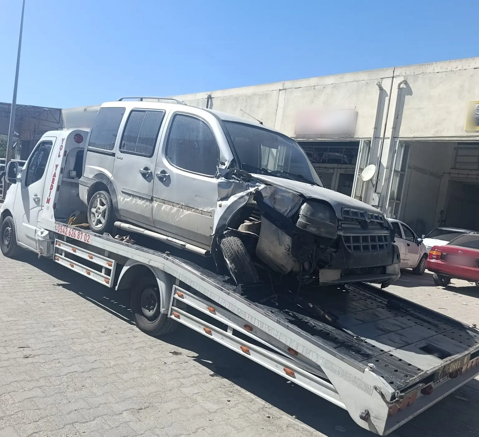 Kazada ön tarafı ezilmiş gri bir hafif ticari araç, beyaz çekicinin kayar platformunda